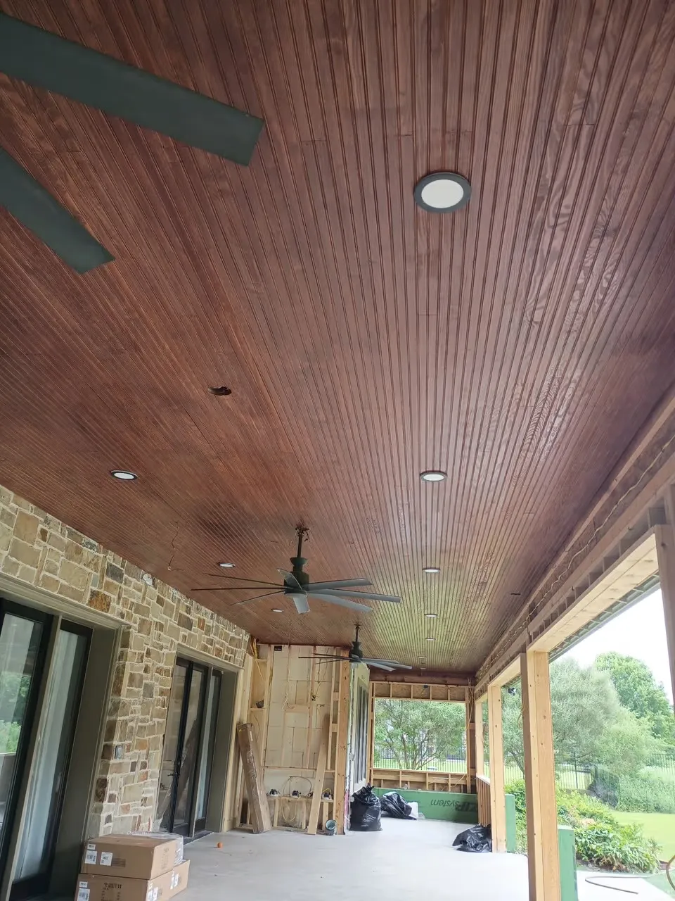 Covered back patio with a stained wood plank ceiling, recessed lights and ceiling fans