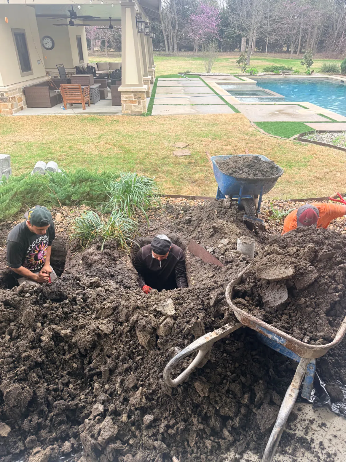 Crew digging by hand beside a covered patio and pool for foundation work