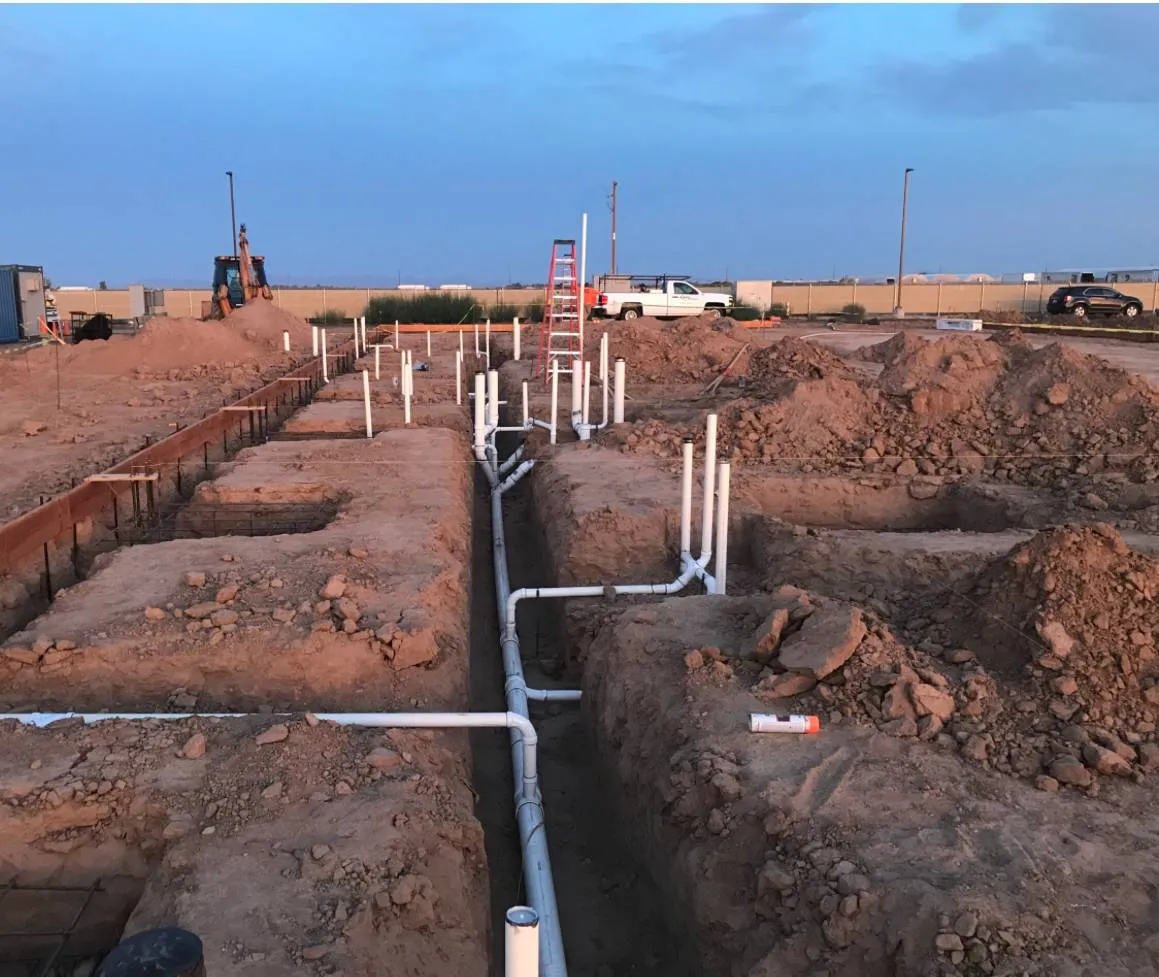 Plumbing rough-in and grade-beam trenches on a new foundation at dusk