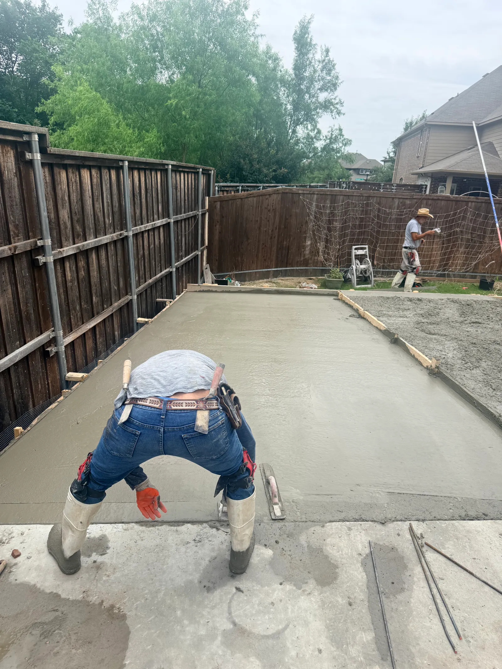 Finisher floating a freshly poured concrete slab in a fenced backyard