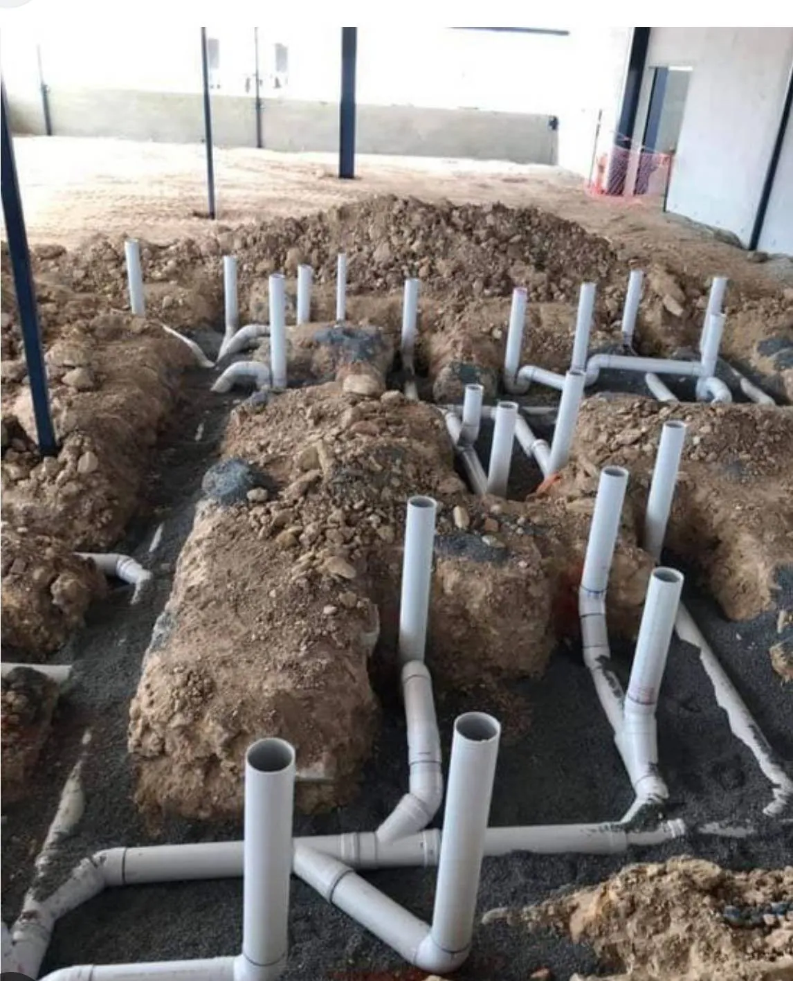 White PVC drain lines stubbed up through the soil before a slab is poured